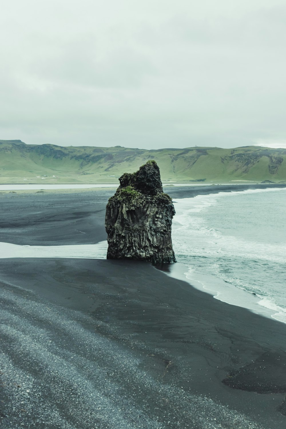 a black sand beach with a rock sticking out of the water