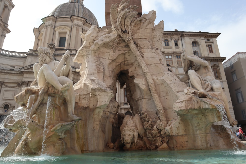 a water fountain with statues and a clock tower in the background