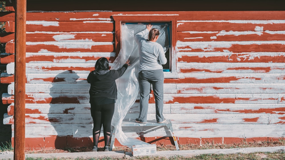 two people are painting a red and white house