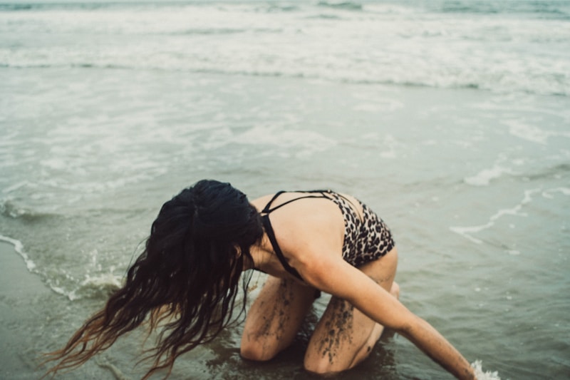 a woman kneeling in the water on a beach