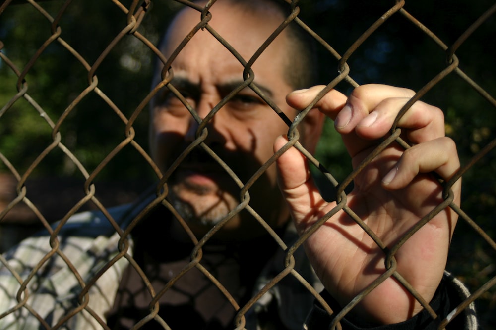 um homem atrás de uma cerca de elo de corrente fazendo um rosto