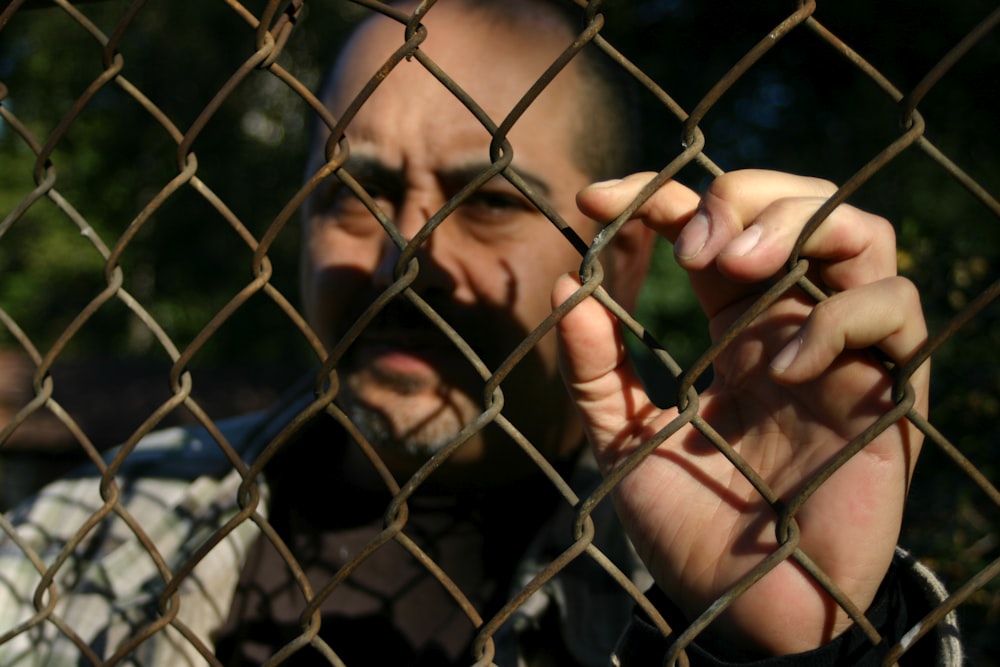 a man behind a chain link fence making a face