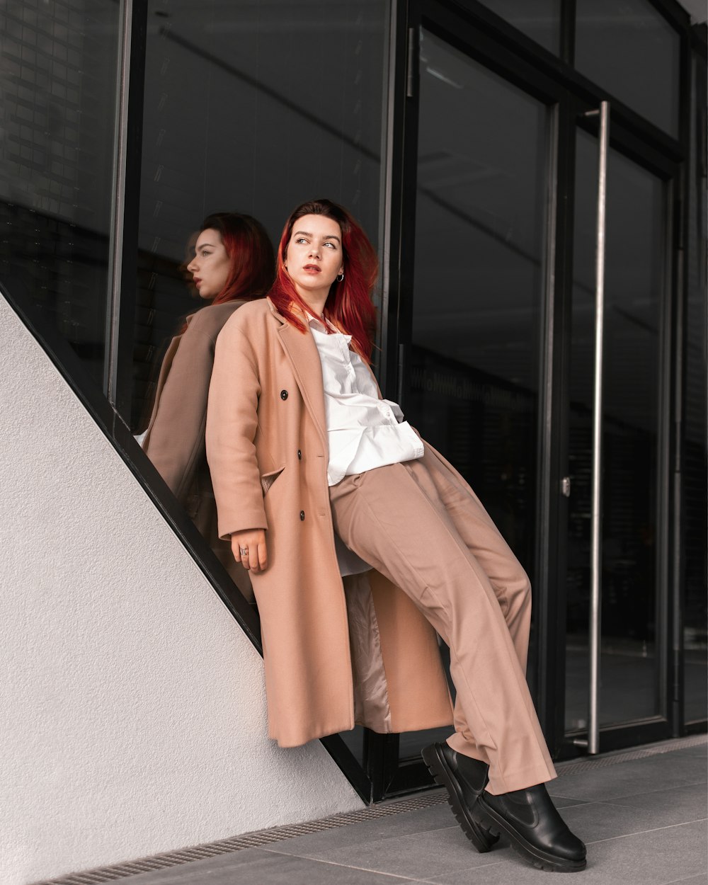 a woman in a trench coat leaning against a wall