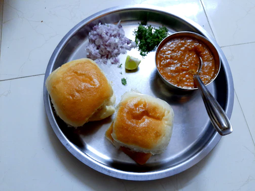 A colorful plate of pav bhaji served with buttered buns and a wedge of lemon on the side.
