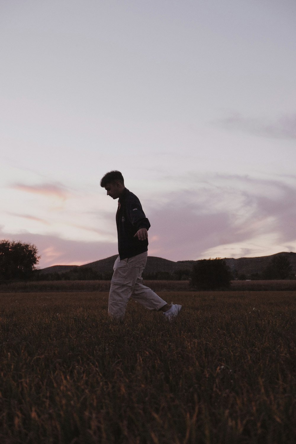 a man walking through a field at sunset