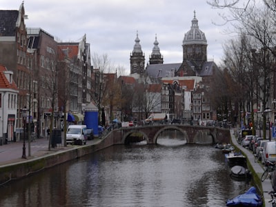Amsterdam canal city - street photography from Holland. A street view over the old canal with in the background the towers of the old church Sint Nicolas, located at the border of the red light district - downtown. The canal water is reflecting the gray sky and the house facades in winter colors. Free pic photo of churches in Amsterdam city, pictures of The Netherlands by Dutch photographer Fons Heijnsbroek.