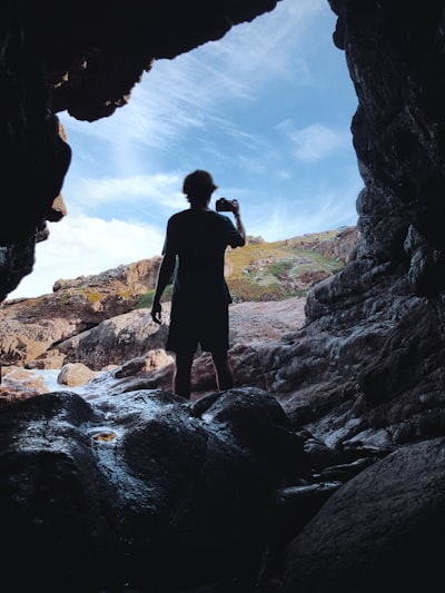 a man standing in a cave looking at the water
