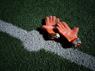 Pair of sturdy cricket gloves with fiery orange accents displayed on a wooden surface.