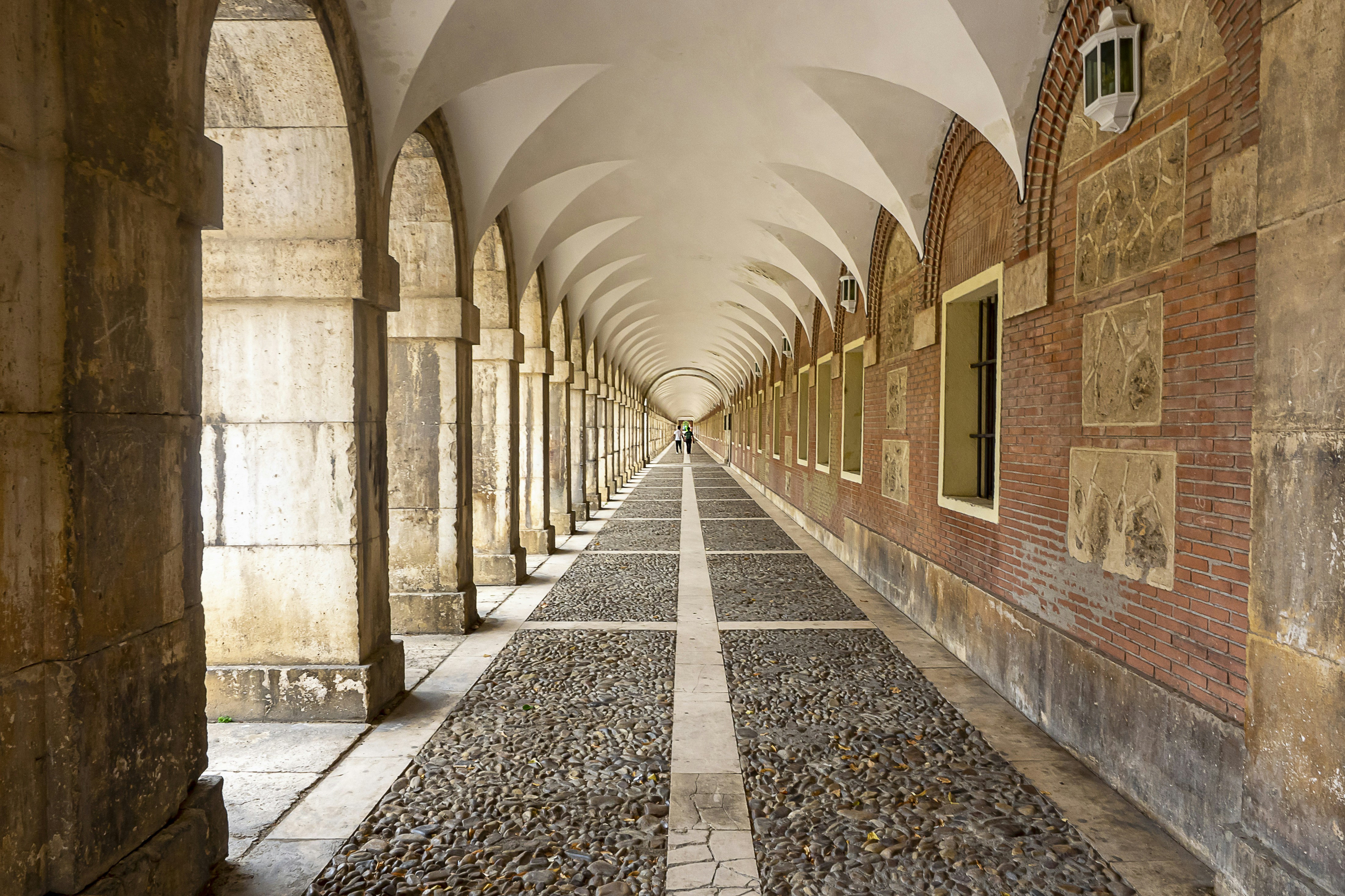 a long hallway with arches and cobblestones on both sides, Porches del Palacio Real de Aranjuez, España