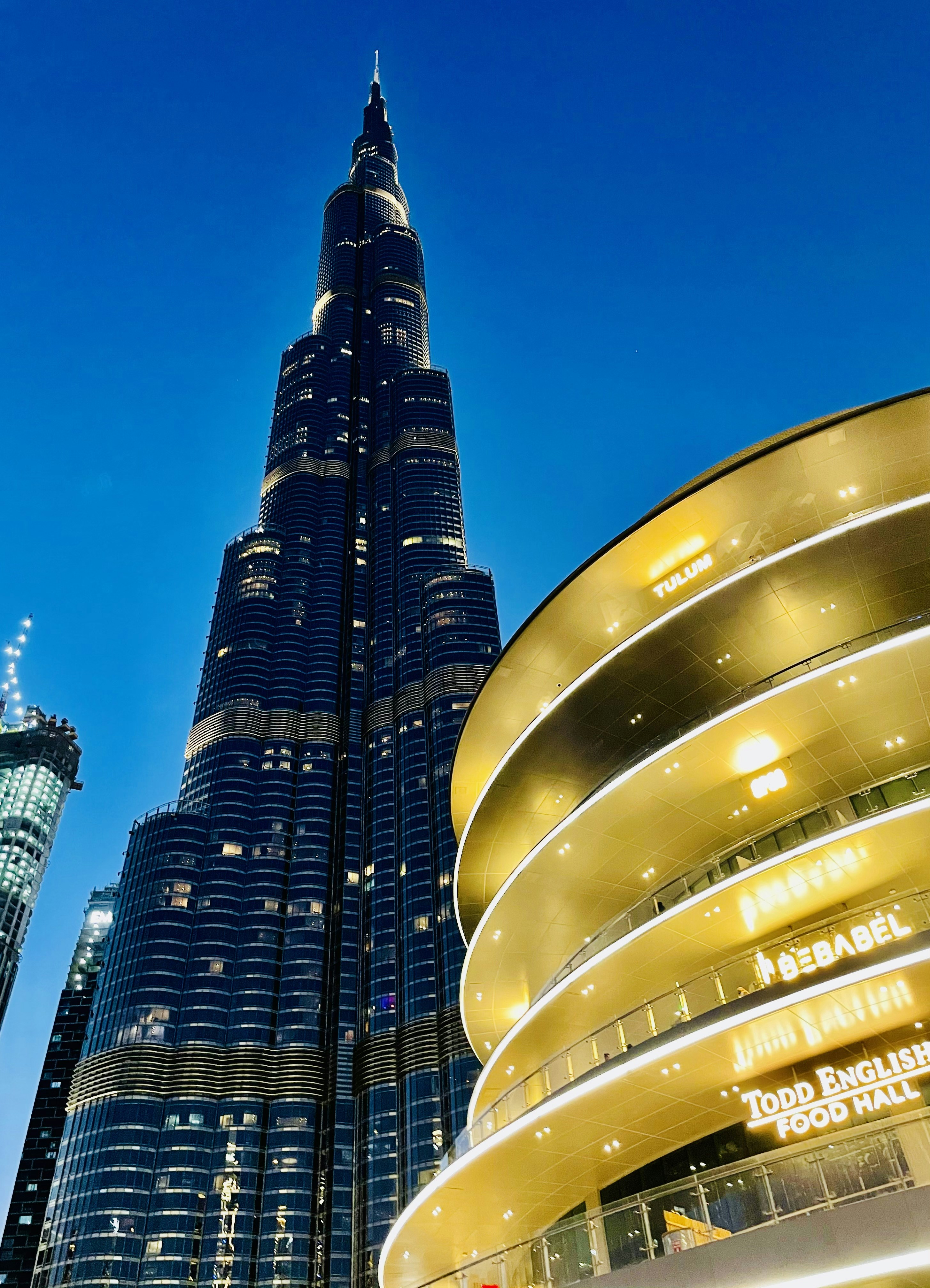 Sky villa aerial view of Abu Dhabi at night, dark cityscape, glowing amber towers, deep blue sky, cinematic shadows