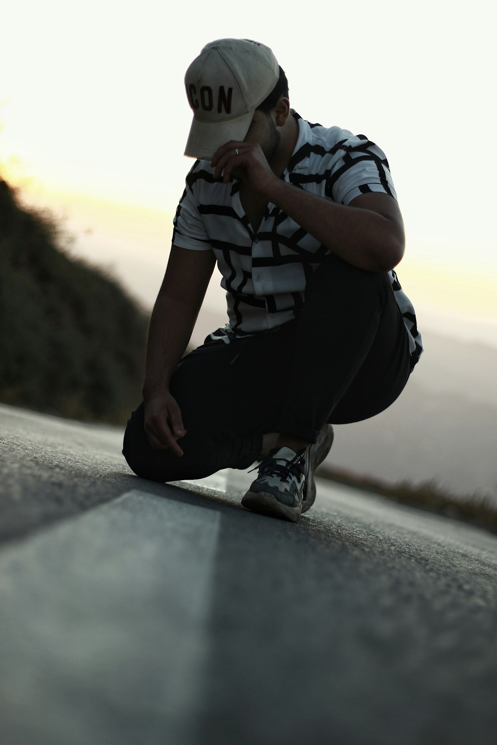 a man sitting on the side of a road wearing a hat