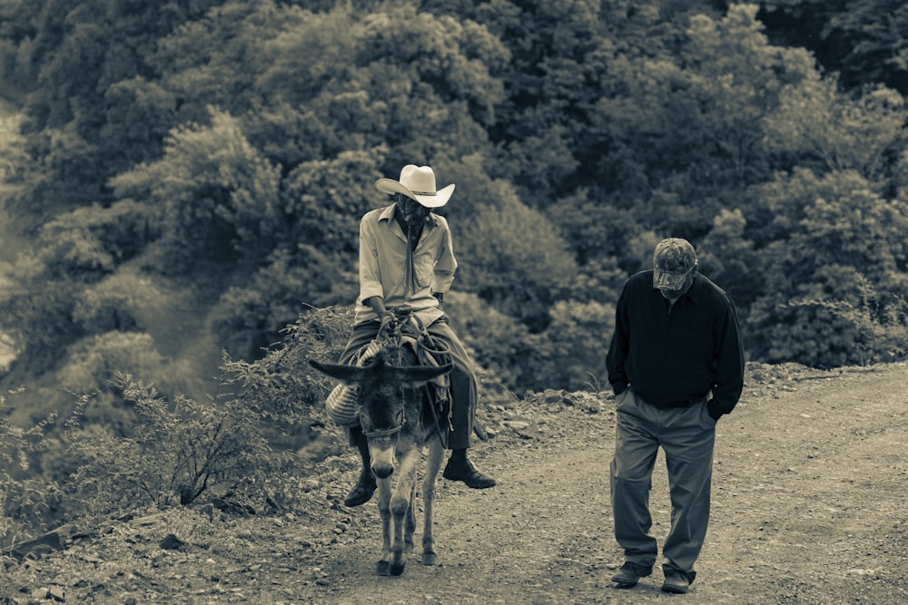 a man walking down a dirt road next to a horse