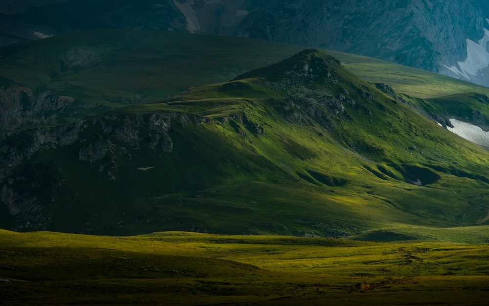 a green mountain range with snow capped mountains in the background