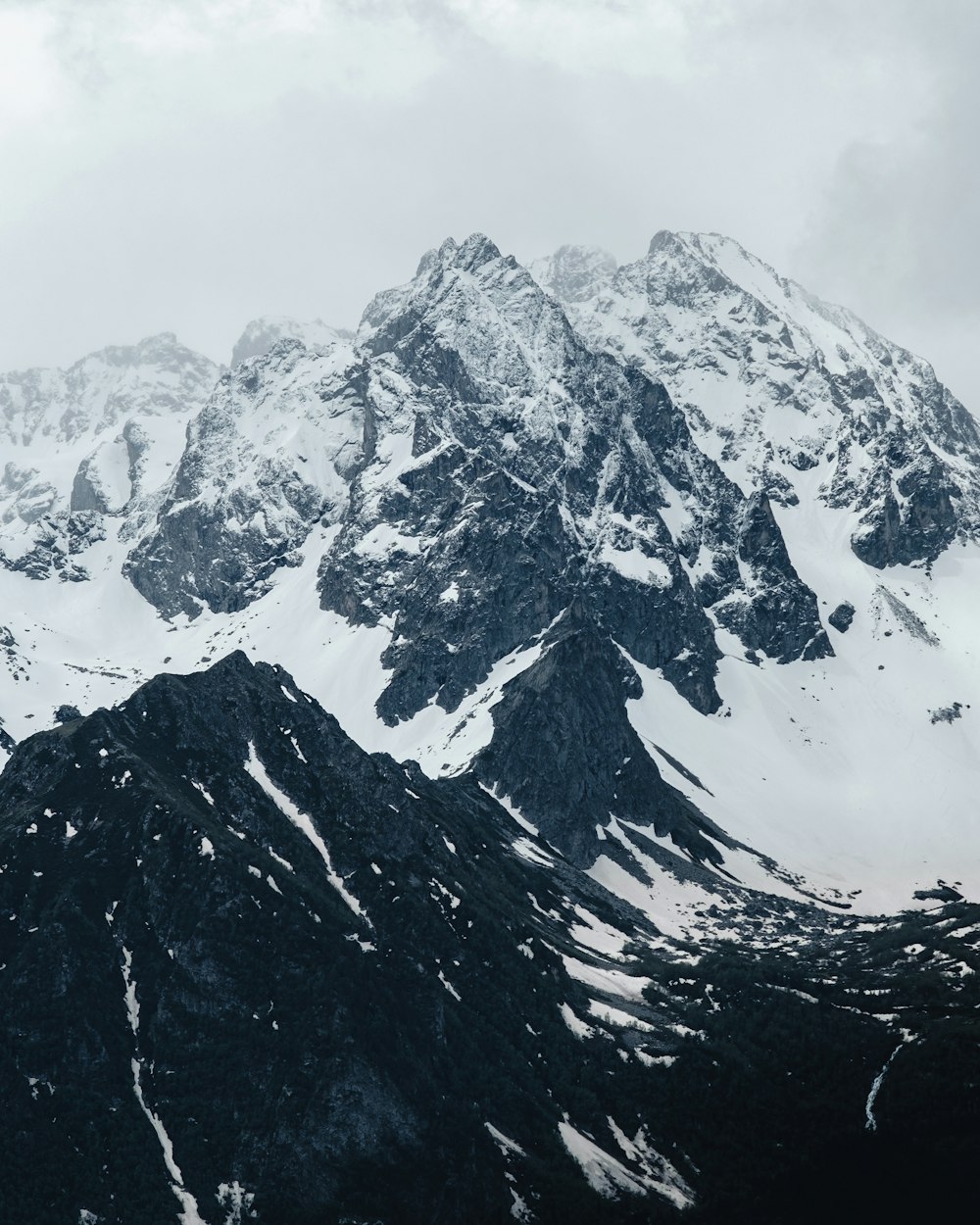 a mountain range covered in snow under a cloudy sky