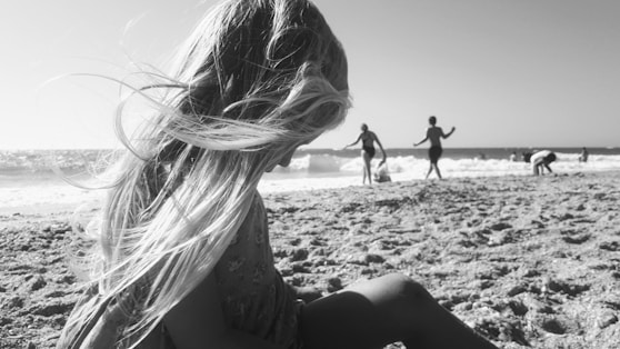 a girl sitting on the beach with her hair blowing in the wind