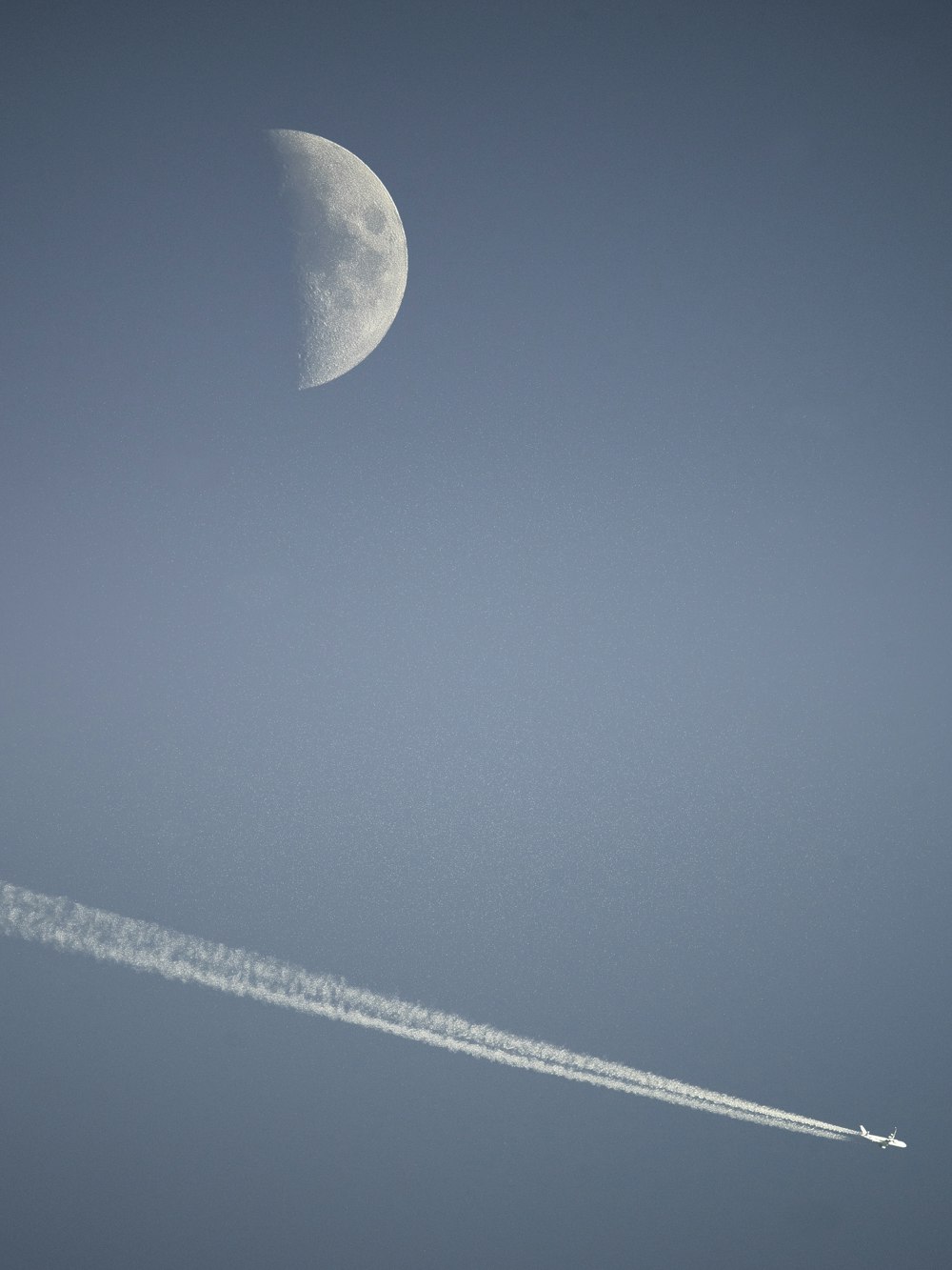 a plane flying in the sky with a half moon in the background