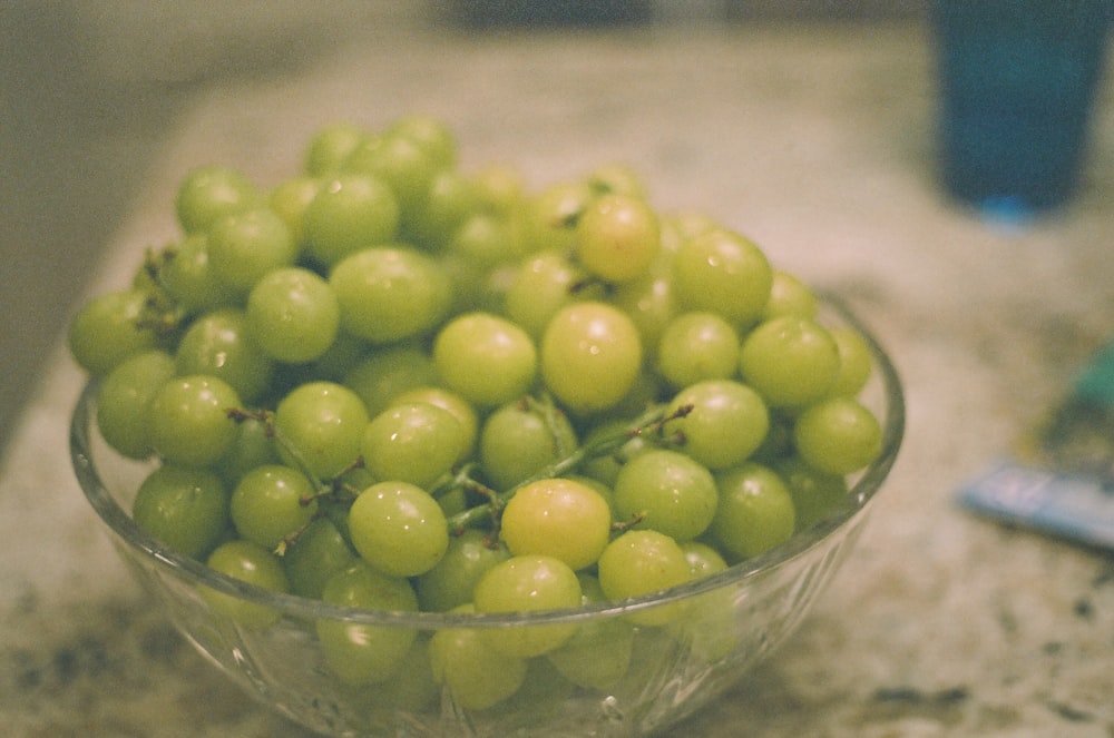 a glass bowl filled with green grapes on top of a counter