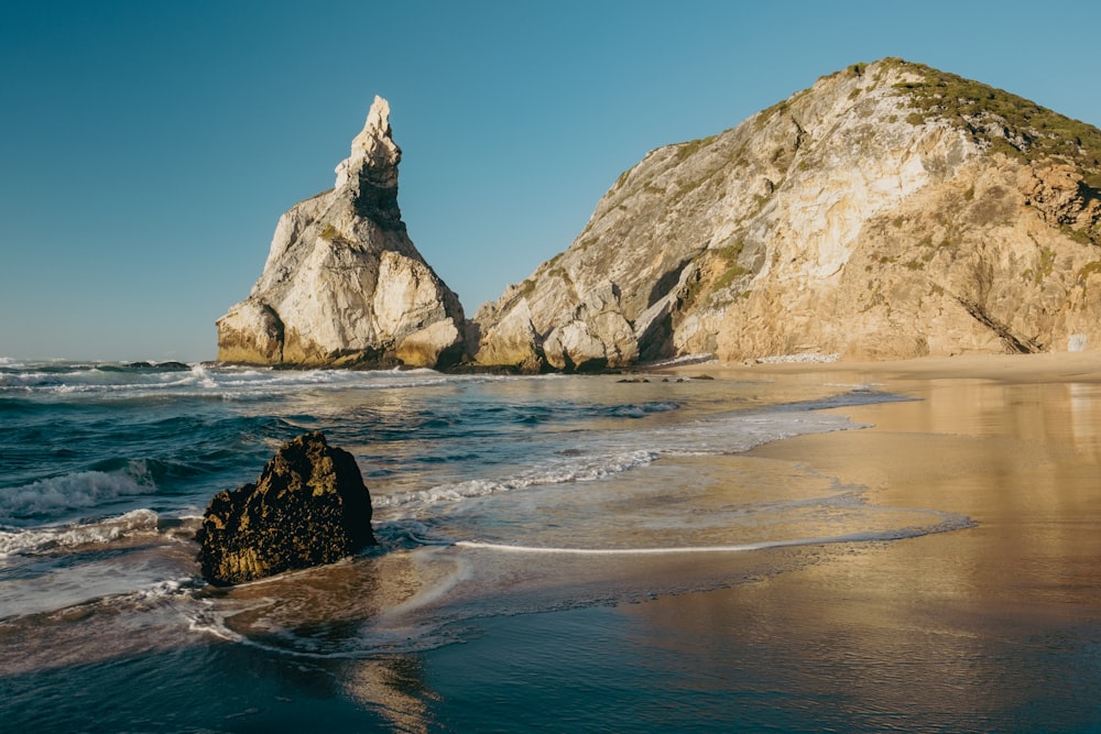 a large rock sticking out of the ocean next to a beach