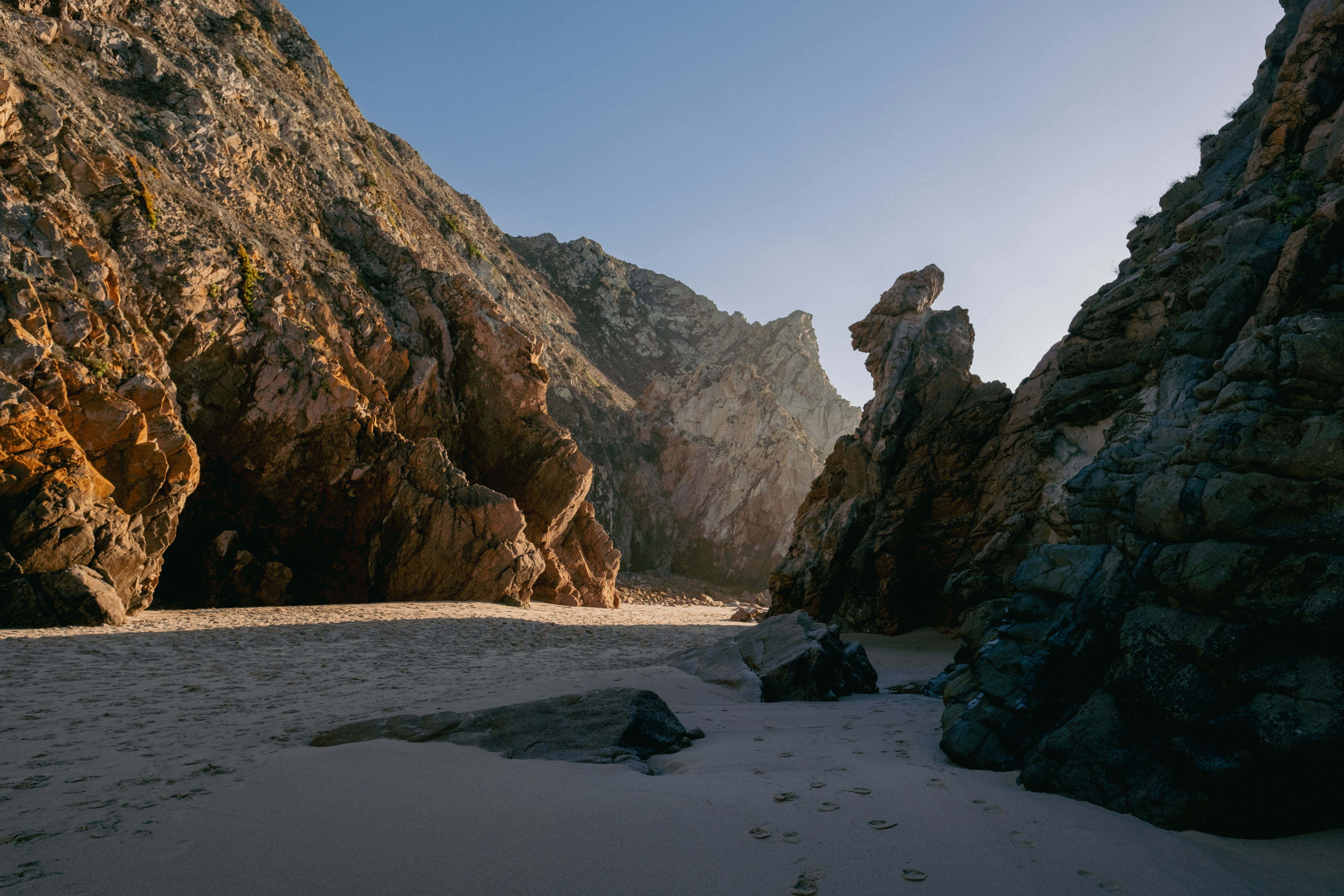 a sandy beach next to a rocky cliff, 