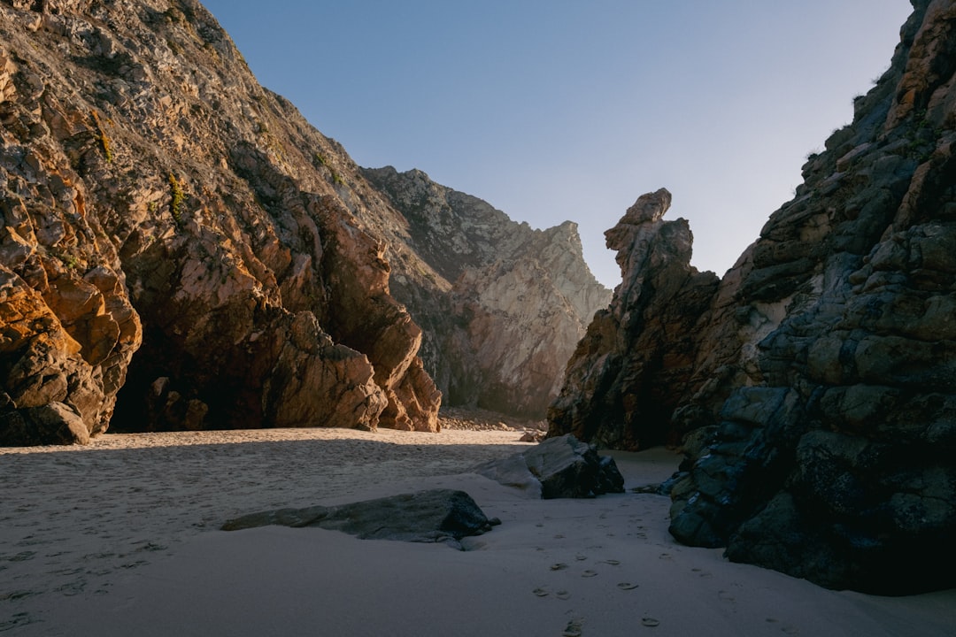 a sandy beach next to a rocky cliff,