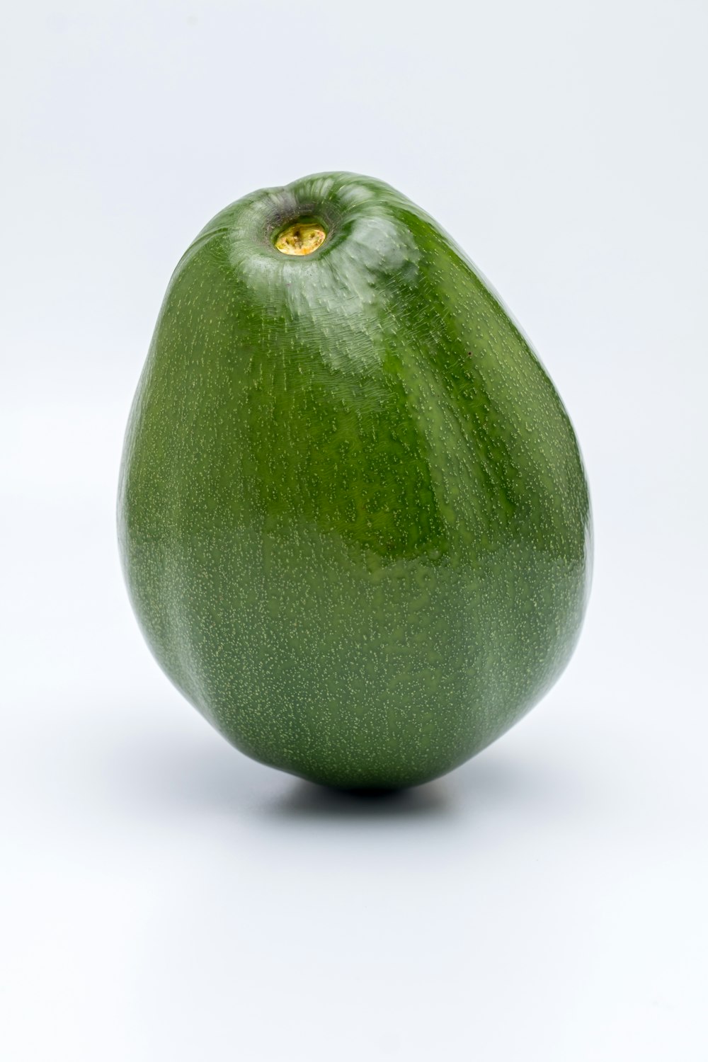 a green apple with a yellow eye sitting on a white surface