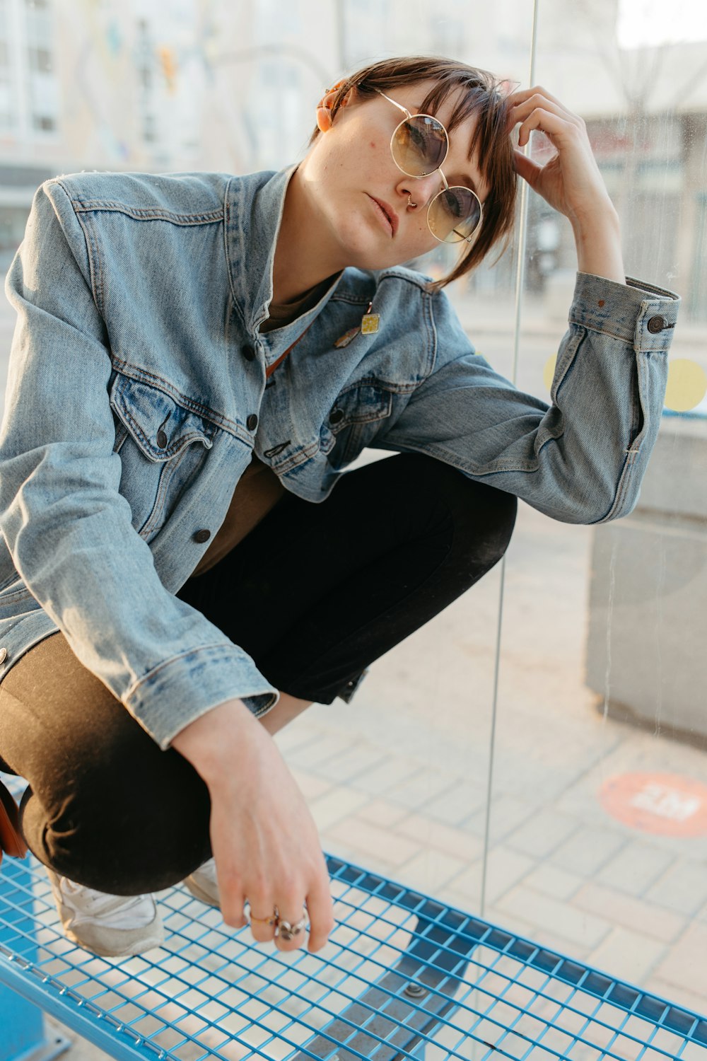 a woman in a jean jacket and sunglasses sitting on a bench