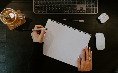 a person writing on a notebook next to a keyboard