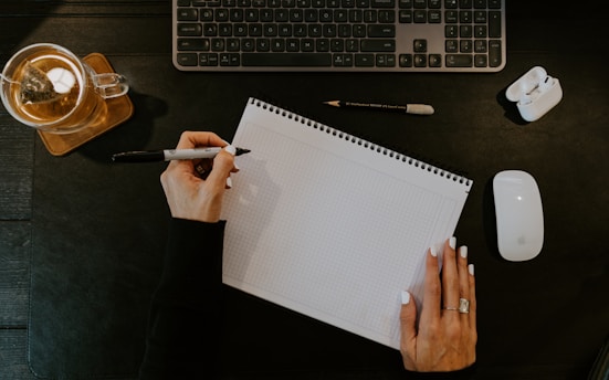 a person writing on a notebook next to a keyboard