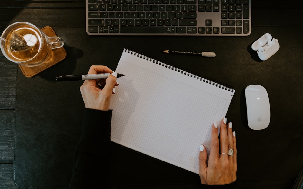 a person writing on a notebook next to a keyboard