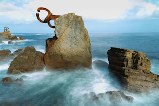a large rock with a sculpture sitting on top of it next to the ocean