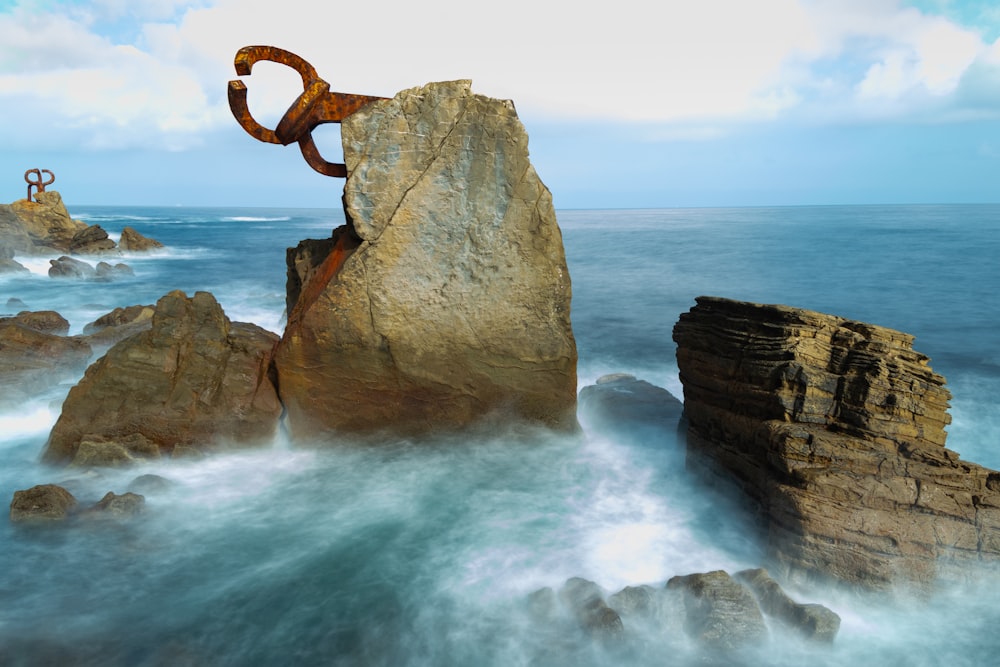 Ein großer Felsen mit einer Skulptur, die neben dem Meer sitzt