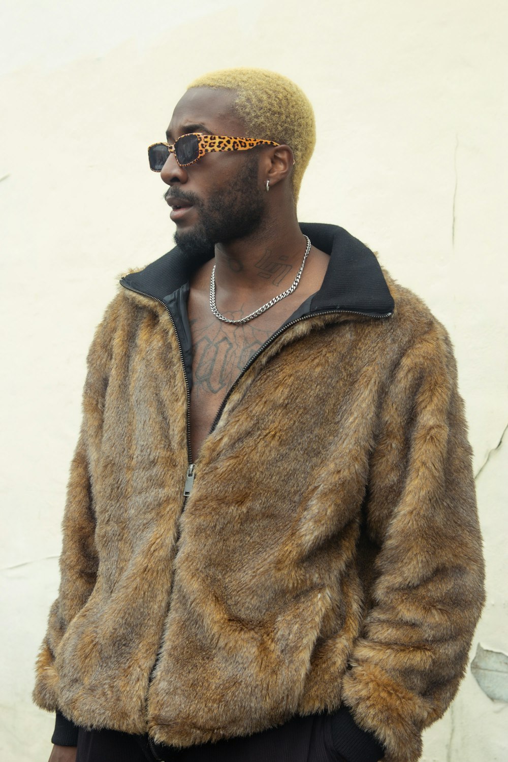 a man wearing a jacket and sunglasses standing in front of a wall