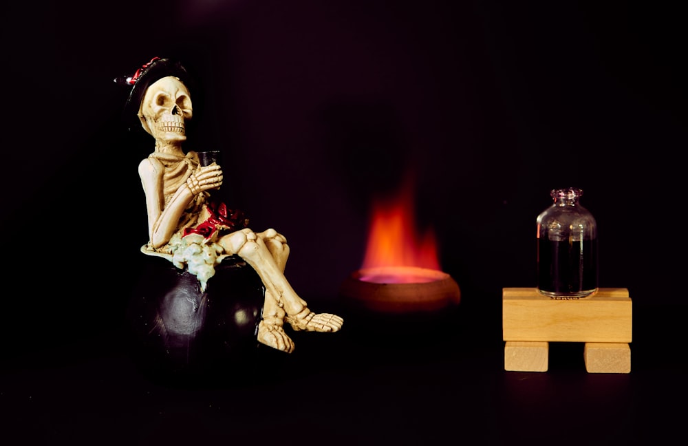 Un esqueleto sentado encima de una bola junto a un fuego