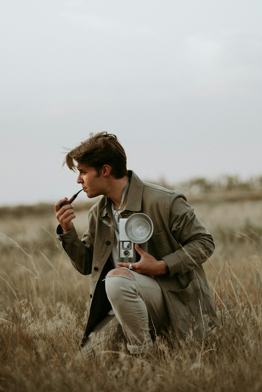a man kneeling in a field holding a camera and a magnifying glass