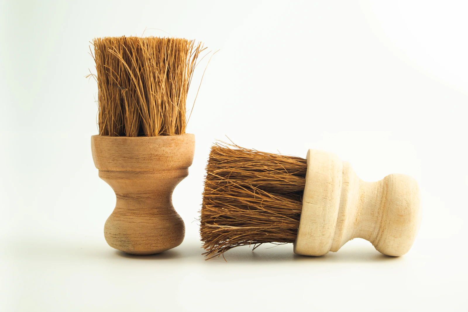 Two wooden-handled scrubbing brushes with natural bristles on a plain white surface