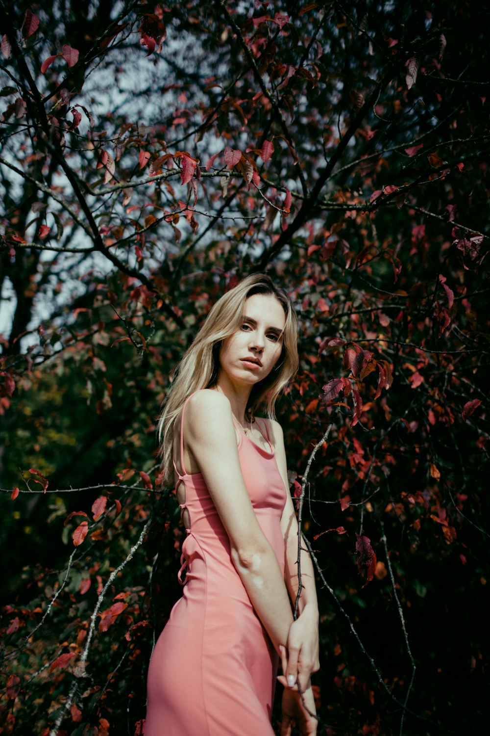 a woman in a pink dress standing in front of a tree