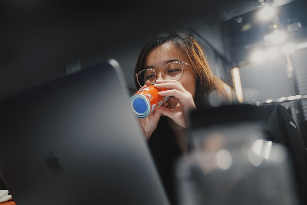 a woman drinking from a cup in front of a laptop