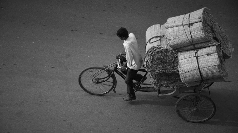 a man riding a bike with a load of hay on the back of it