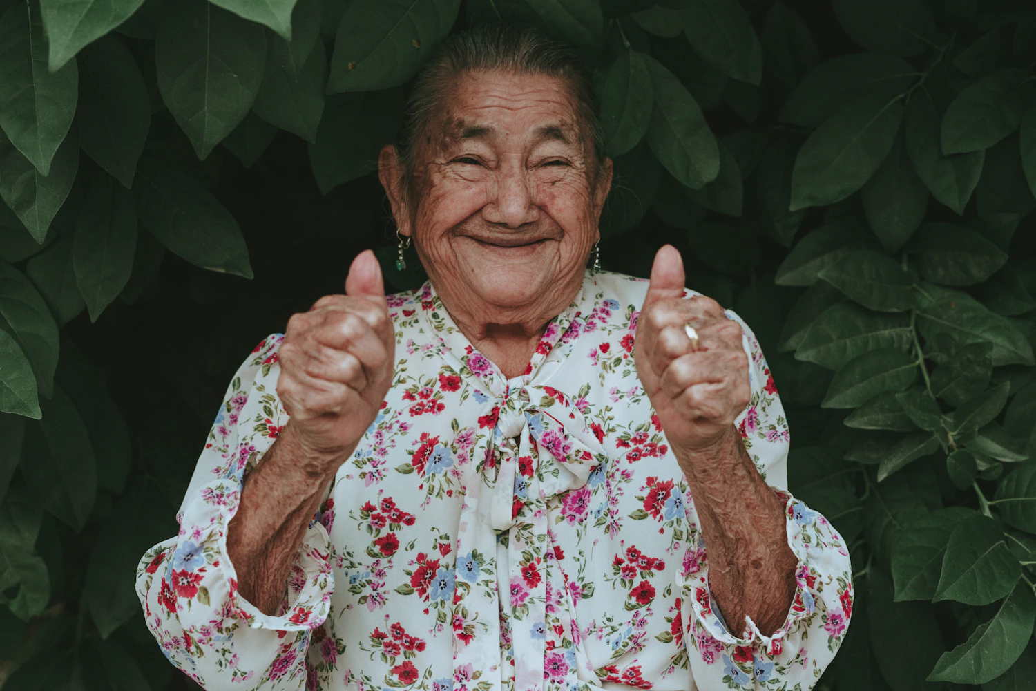 An older woman in a flowered blouse giving two thumbs up