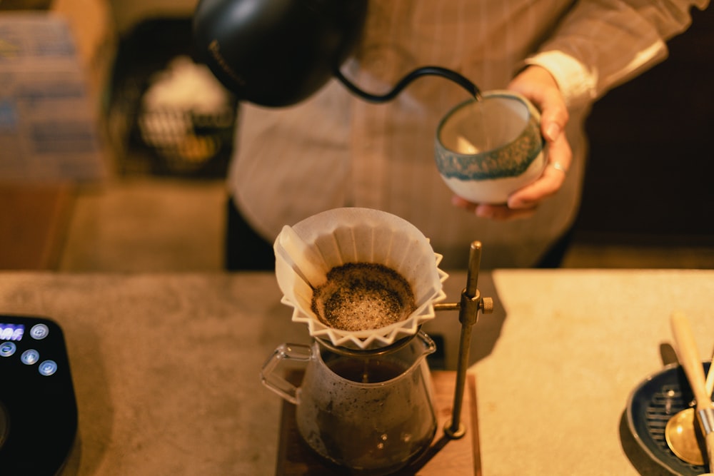 a person pours a cup of coffee into a coffee pot