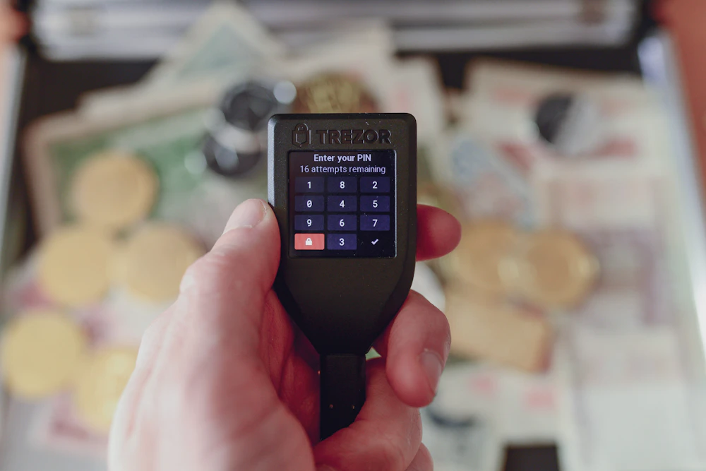 Trezor hardware wallet held in a hand with cryptocurrency imagery in the background