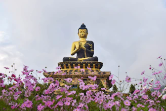 a buddha statue sitting on top of a statue surrounded by purple flowers