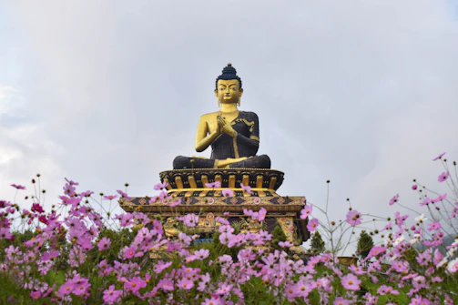 a buddha statue sitting on top of a statue surrounded by purple flowers