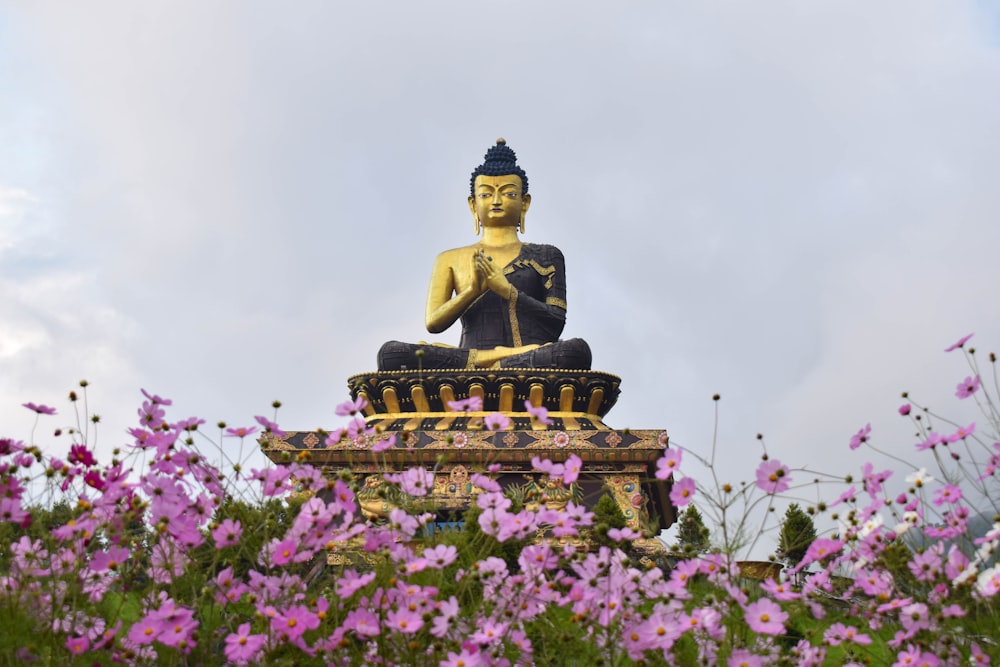 a buddha statue sitting on top of a statue surrounded by purple flowers