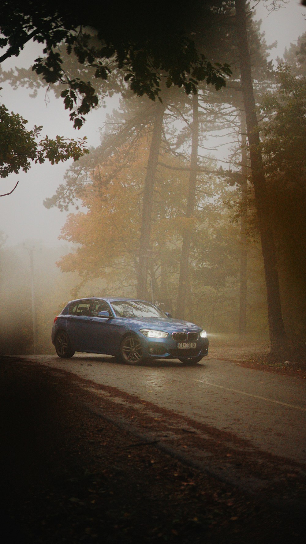 a blue car driving down a road next to a forest