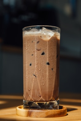 a tall glass filled with liquid sitting on top of a wooden table