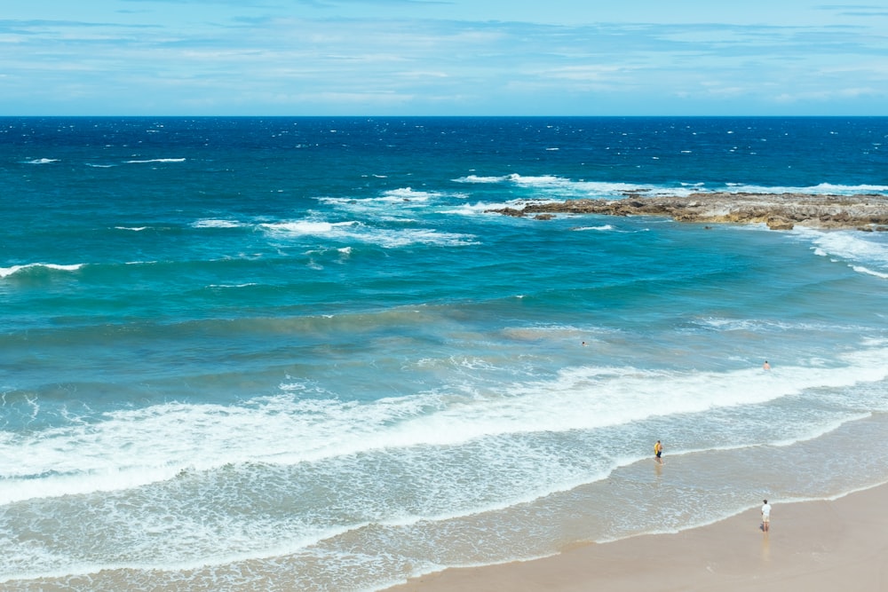 a couple of people standing on top of a sandy beach