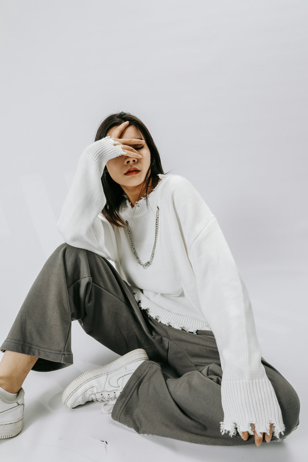 a woman sitting on the ground wearing a white sweater