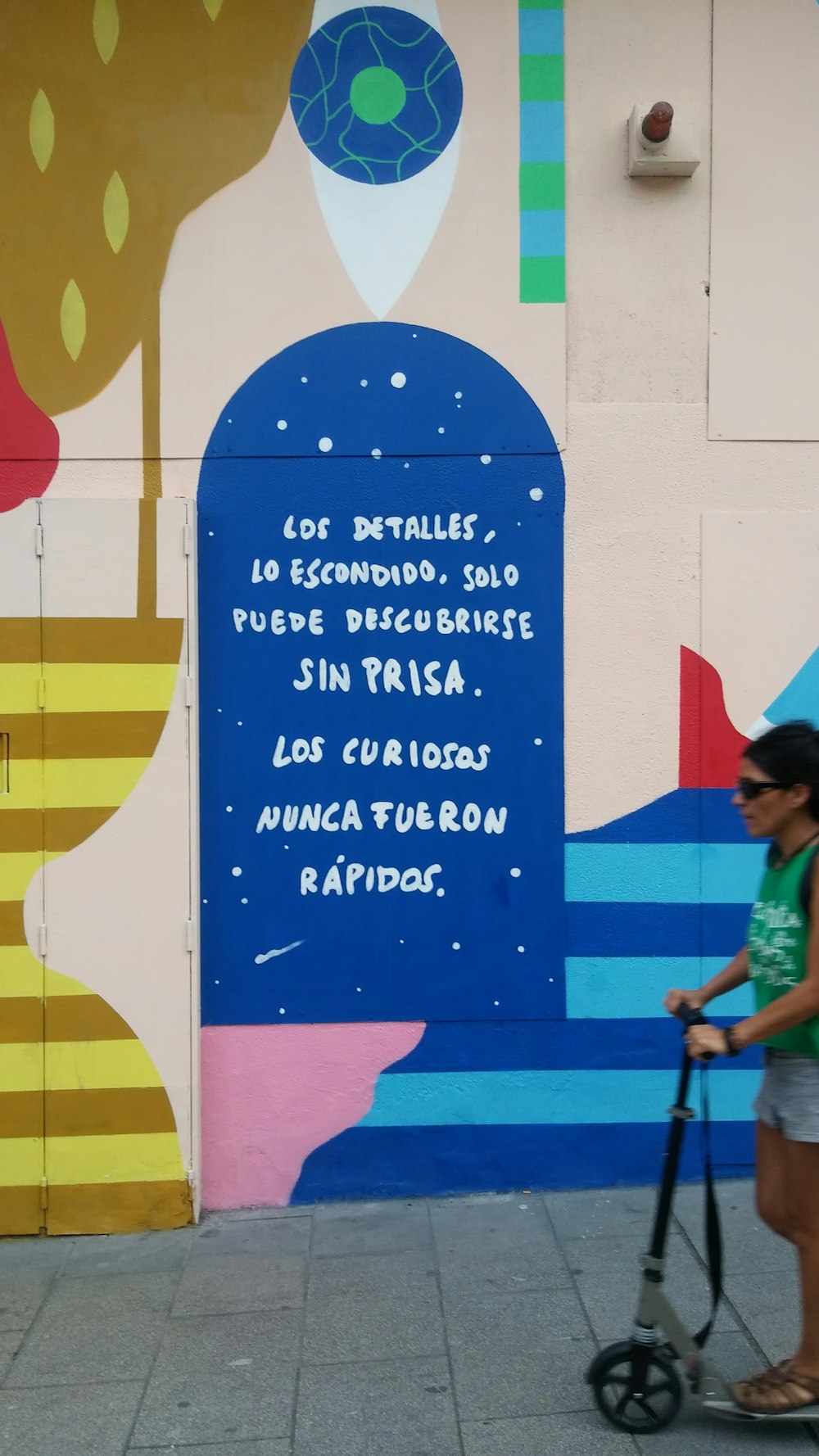 a woman riding a scooter past a colorful wall