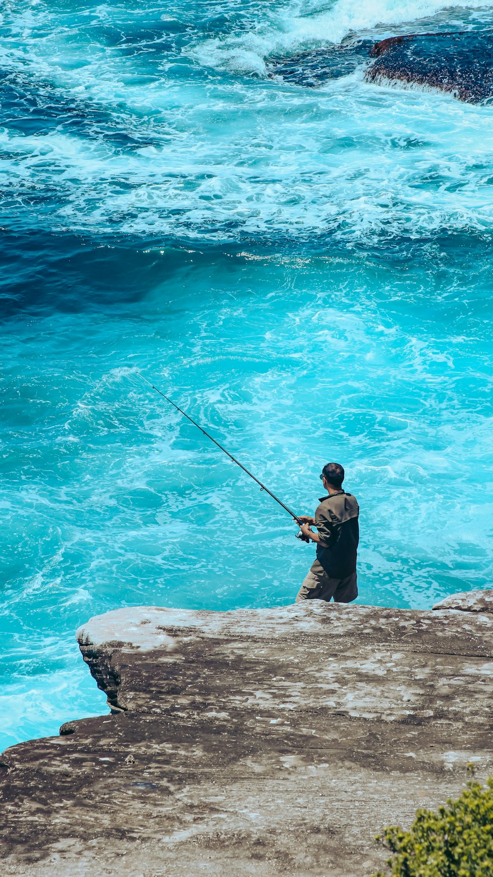 a man sitting on a rock fishing in the ocean